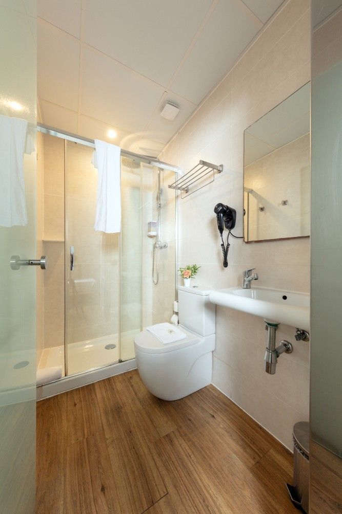 Un baño moderno con ducha con mampara de cristal, inodoro blanco, lavabo de pared, espejo.