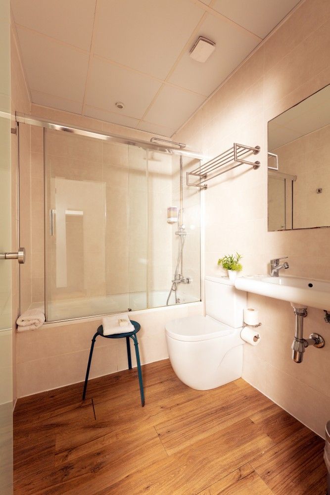 Un baño moderno con suelo de imitación madera, un inodoro blanco, una ducha con mampara de cristal,.