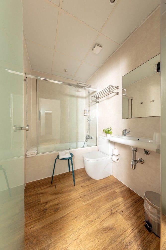 Un baño moderno y bien iluminado con piso de baldosas con apariencia de madera, una ducha con mampara de vidrio, un lavabo.