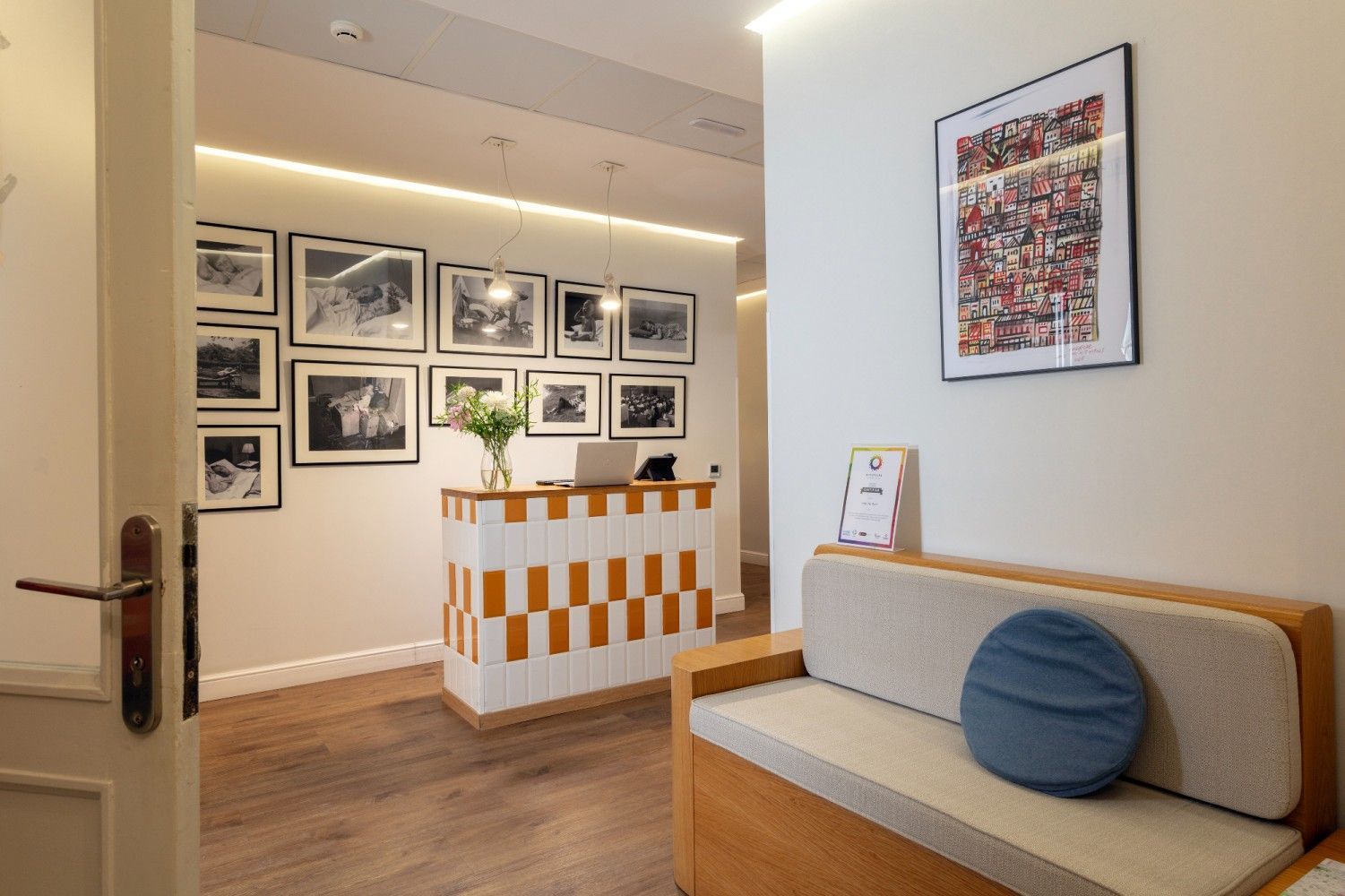 Área de recepción con un escritorio a cuadros naranja y blanco, un sofá beige con una almohada redonda azul.