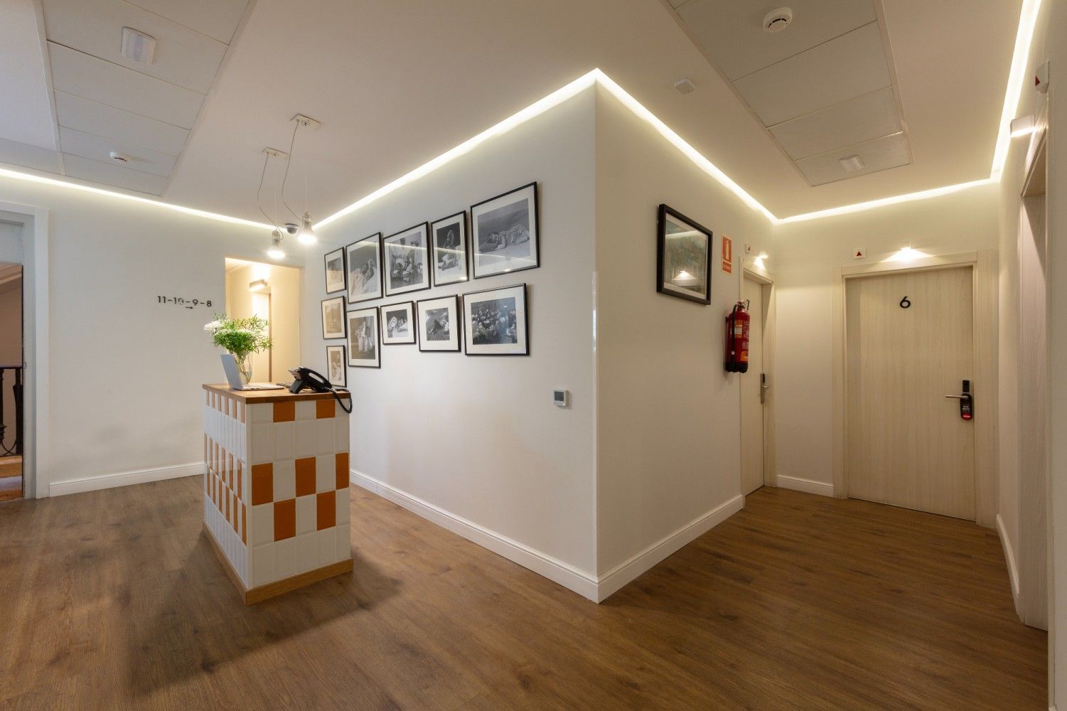 Un área de recepción de hotel con un mostrador estampado, una galería de fotos enmarcadas en la pared, pisos de.