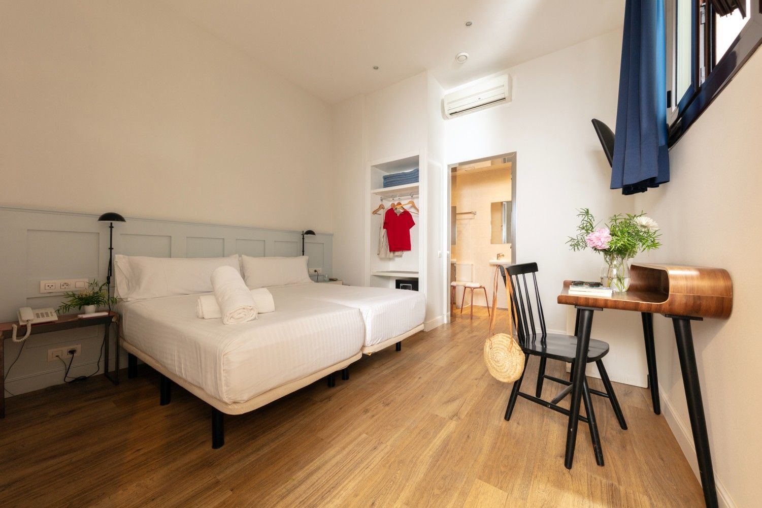 Una habitación de hotel con dos camas individuales blancas, un escritorio de madera con una silla negra.