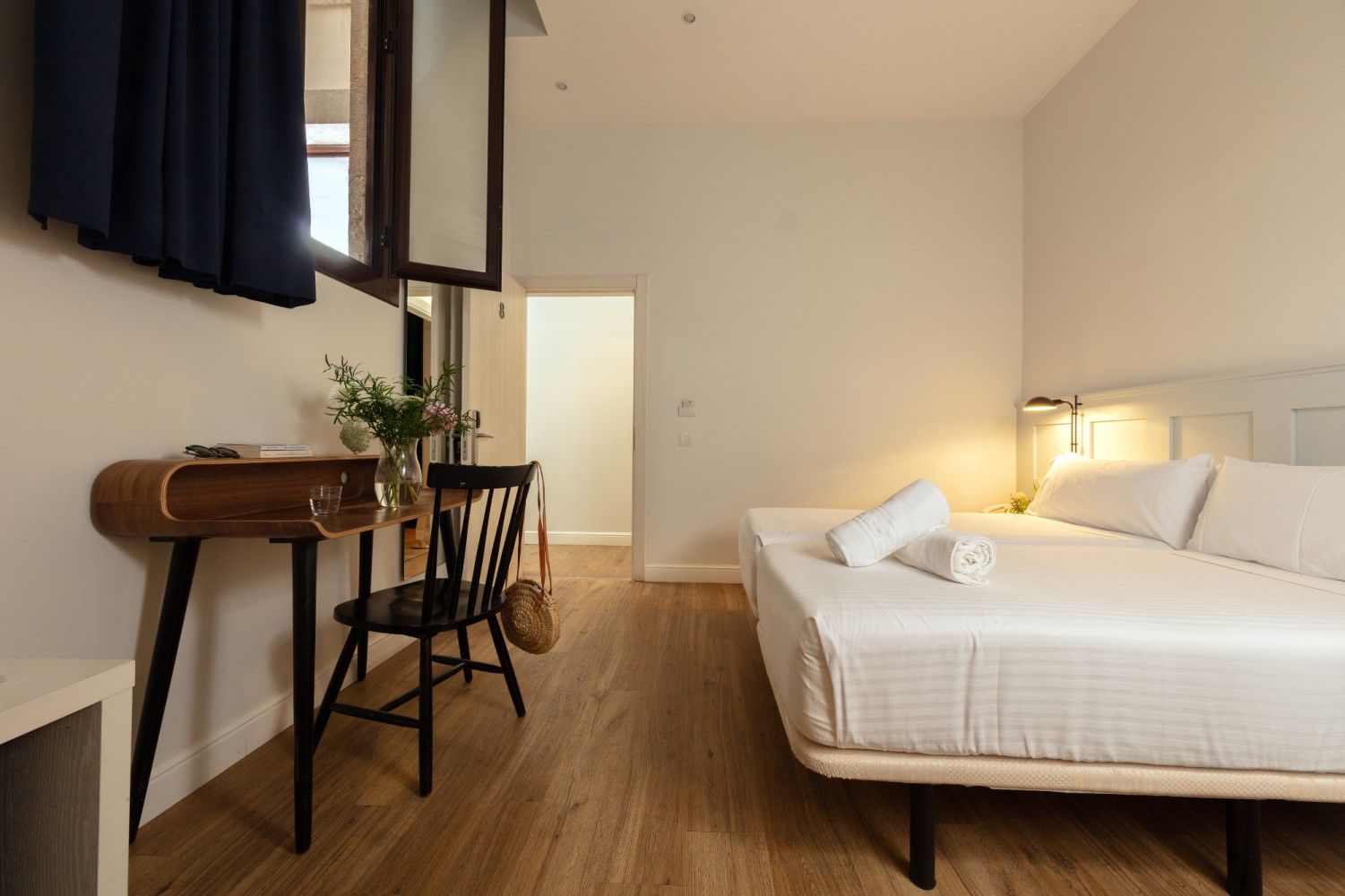 Un dormitorio minimalista con una cama queen, pisos de madera, un pequeño escritorio con una silla..