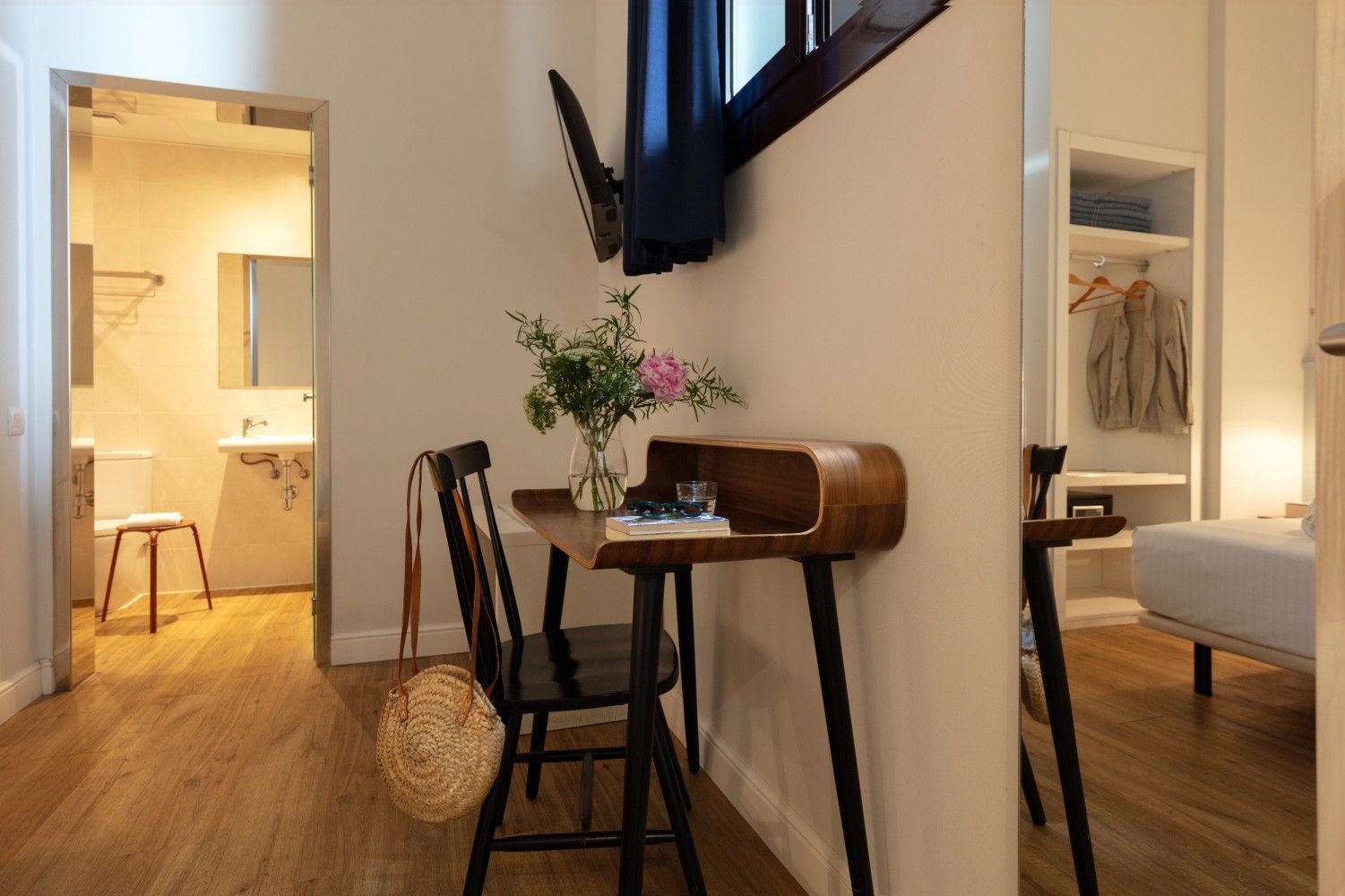 Un escritorio y una silla de madera en una habitación luminosa, con un vistazo a un armario abierto a la derecha.