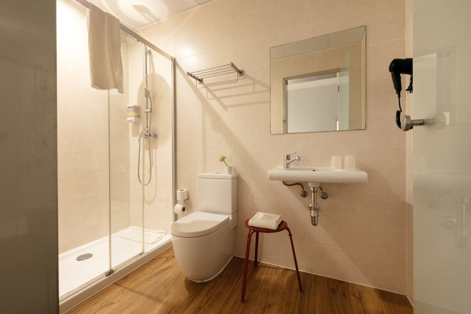 Un baño moderno en tonos claros que cuenta con una ducha de cristal, un inodoro blanco.