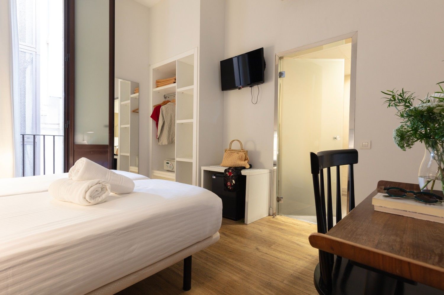 Una habitación de hotel con una cama cuidadosamente hecha, estanterías abiertas.