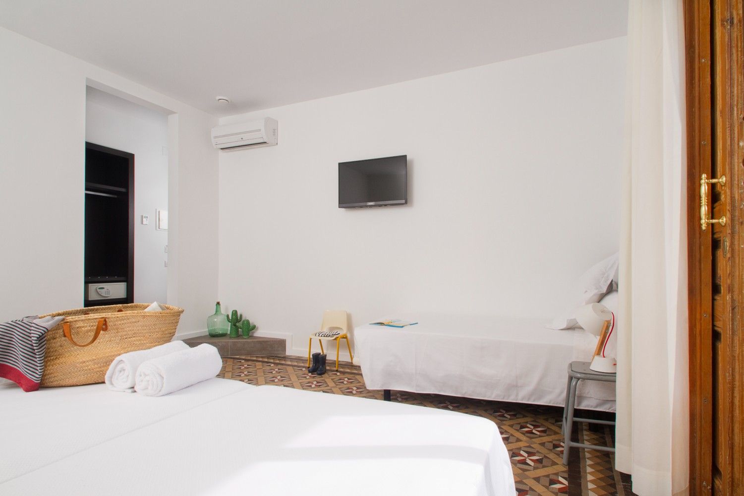 Una habitación de hotel con paredes blancas, dos camas, un televisor colgado, un pequeño aire acondicionado .