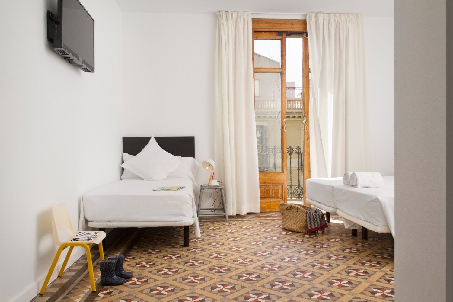 Un dormitorio con dos camas individuales, suelo de baldosas, paredes blancas, una silla amarilla.