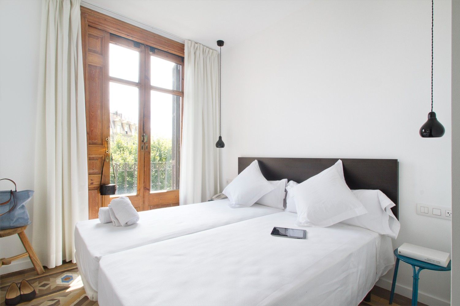 Un dormitorio luminoso con dos camas individuales con sábanas blancas, una puerta de balcón de madera.