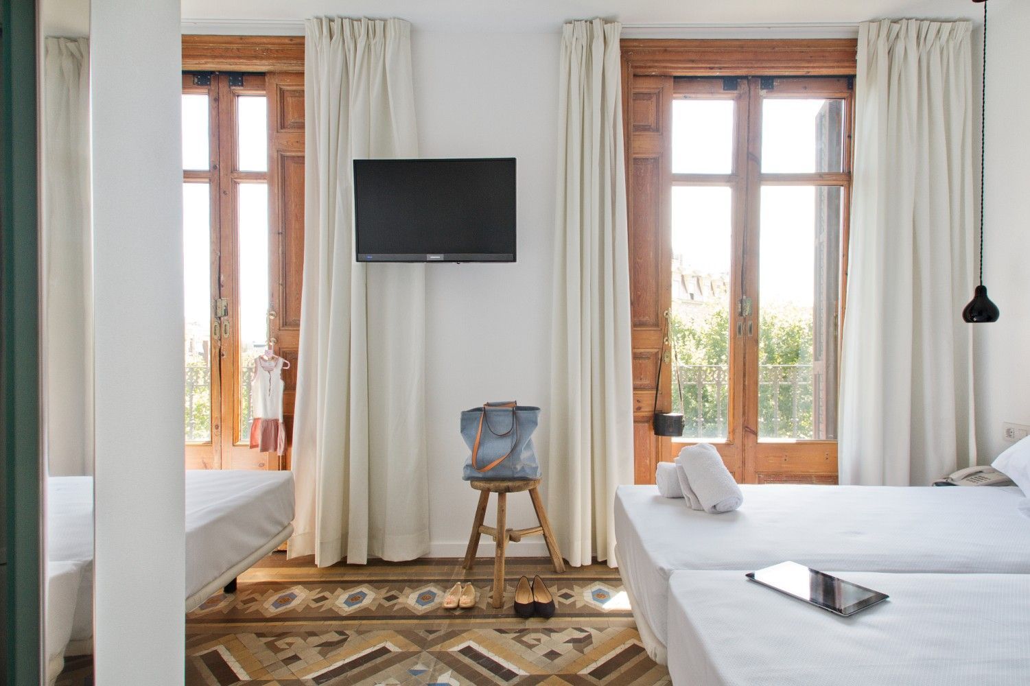 Un dormitorio con dos camas, paredes blancas, cortinas color crema, un televisor colgado en la pared.