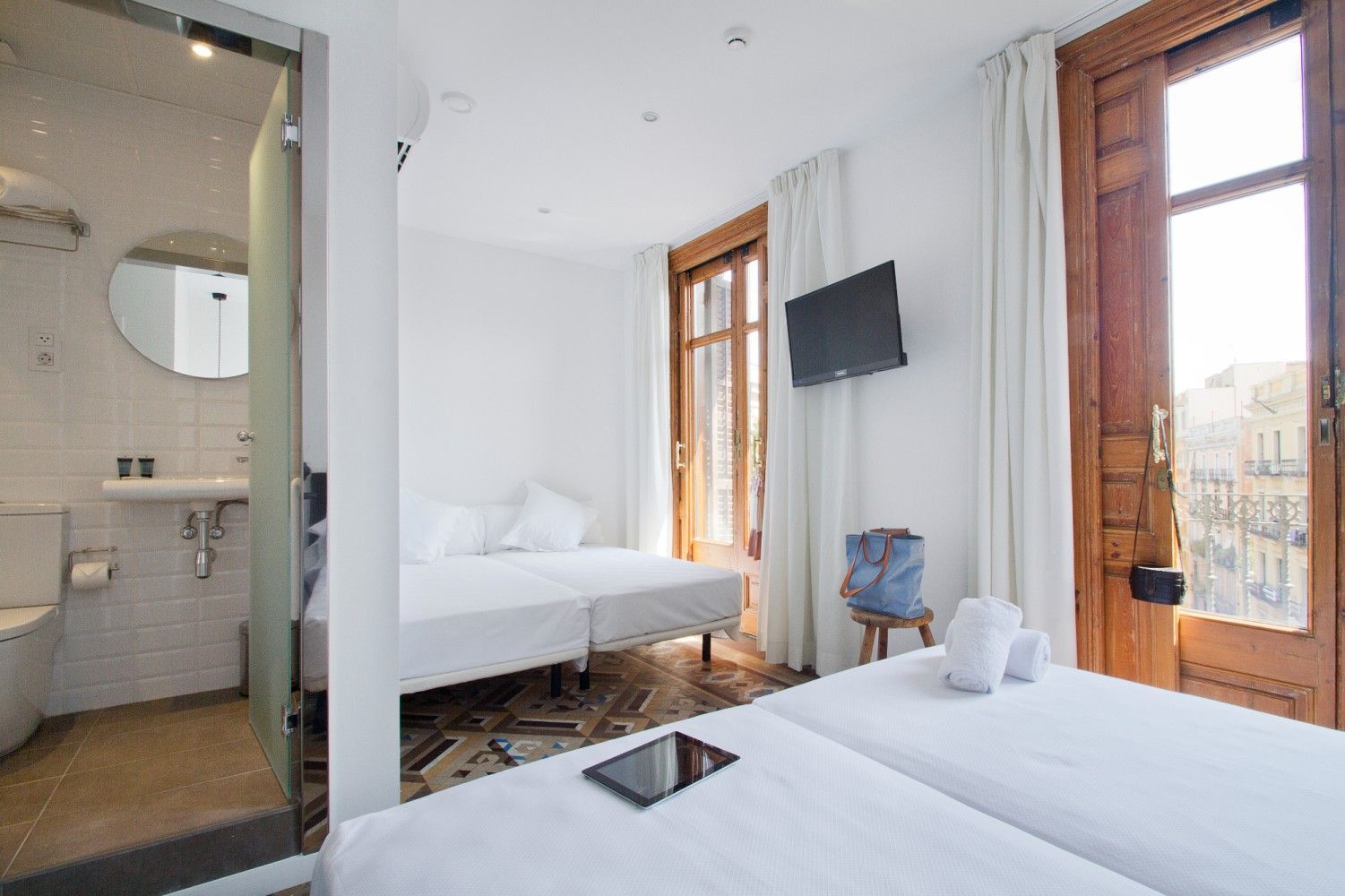 Una habitación de hotel luminosa y minimalista con dos camas individuales, un pequeño televisor montado en la pared .