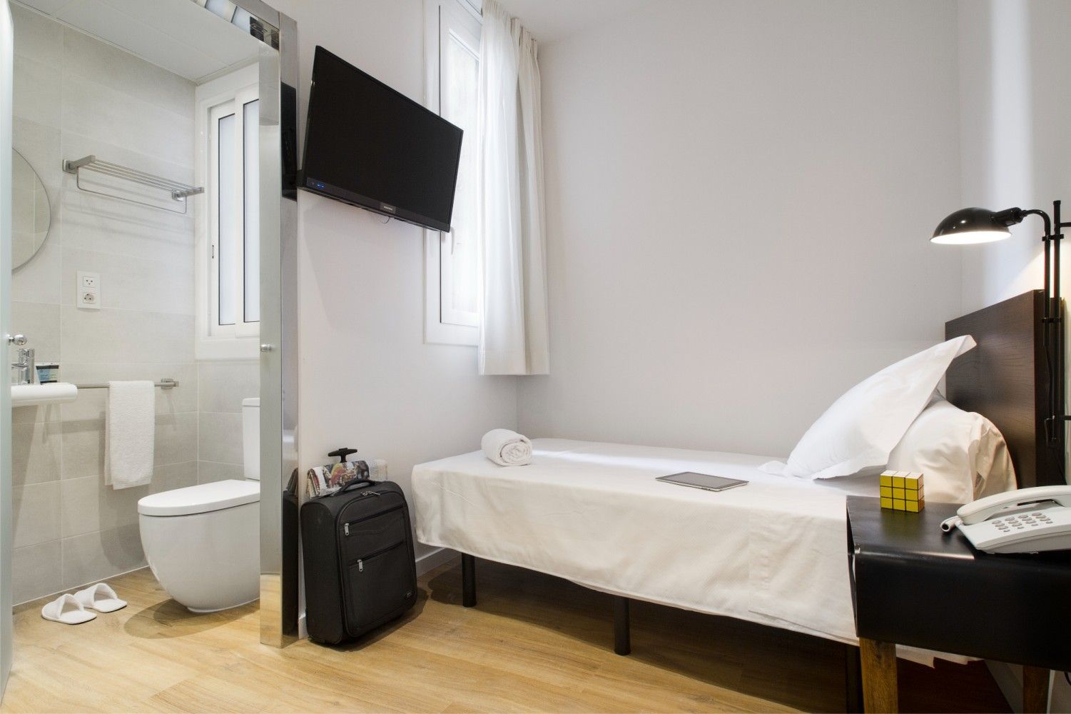 Una habitación de hotel con una cama individual, un televisor de pared, una lámpara de noche.