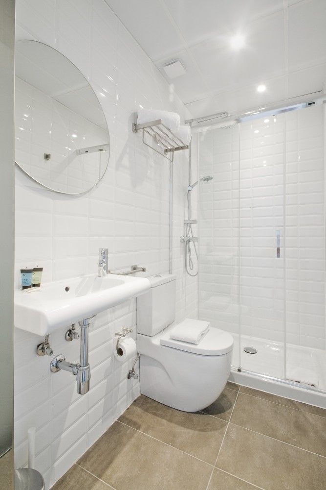 Un baño moderno y limpio con azulejos blancos tipo metro, un lavabo montado en la pared, un espejo redondo.