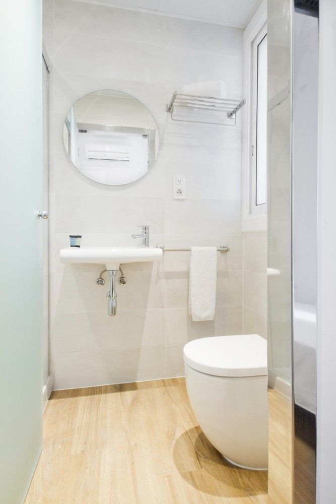 Un baño pequeño y moderno que cuenta con un lavabo blanco montado en la pared, un espejo circular.