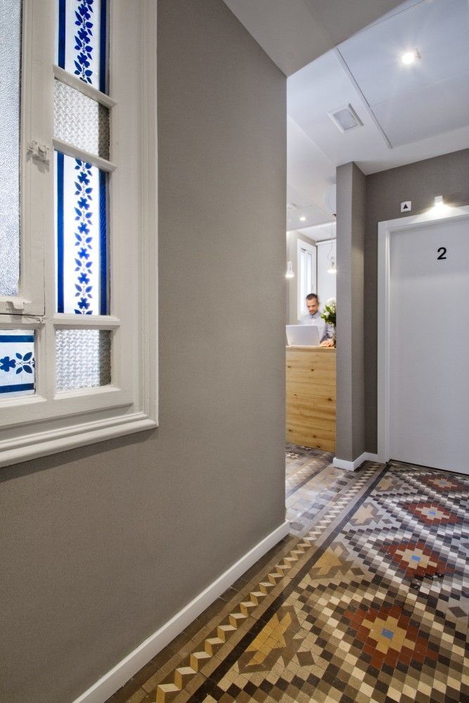 Un pasillo con piso de baldosas con dibujos ornamentados, una puerta blanca marcada con un 