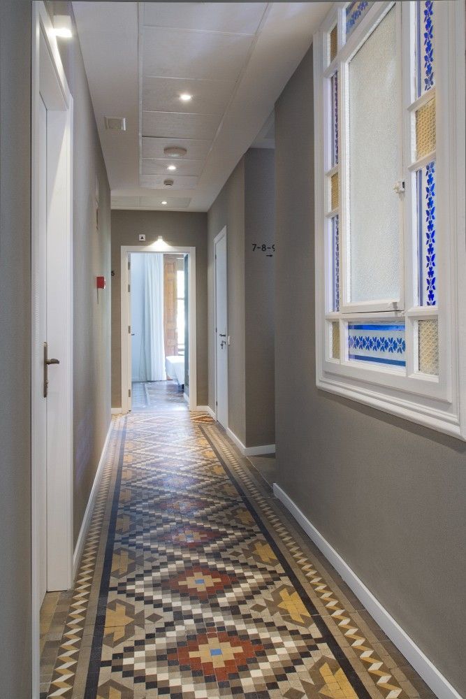 Un pasillo largo con suelo de baldosas estampadas en forma de diamante, paredes neutrales, puertas blancas.