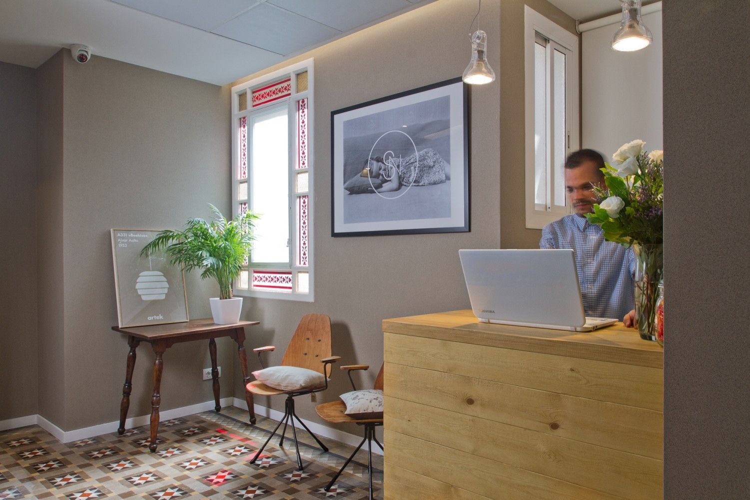 Una persona trabaja en un mostrador de recepción de madera en una habitación con dos sillas, una planta, arte de pared.