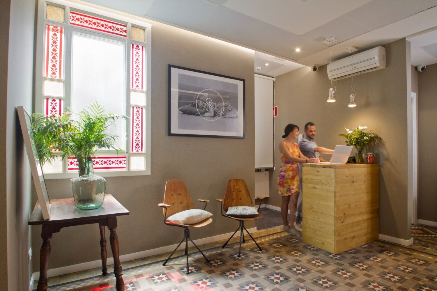 Una mujer y un hombre están de pie frente a un mostrador de recepción de madera en una habitación con pisos de baldosas .