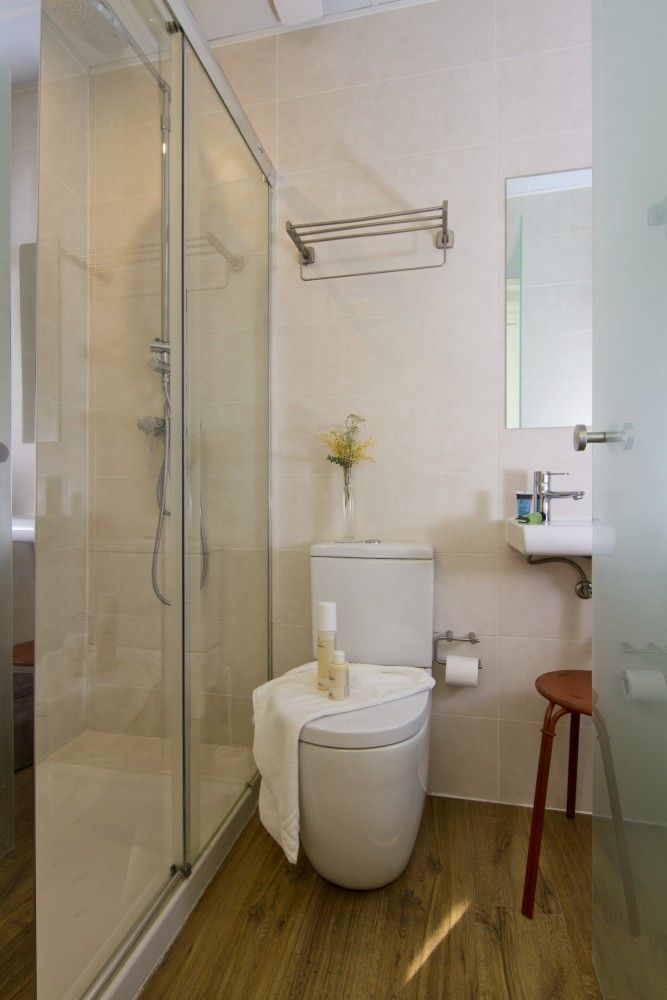 Un baño con ducha con mampara de cristal, un inodoro blanco con una toalla encima, un lavabo montado en la pared.