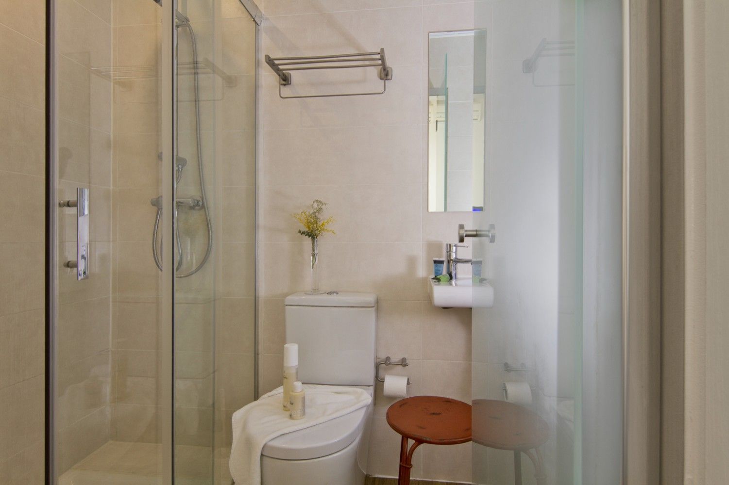 Un baño compacto con una cabina de ducha de cristal, un inodoro blanco con toalla, un lavabo montado en la pared.