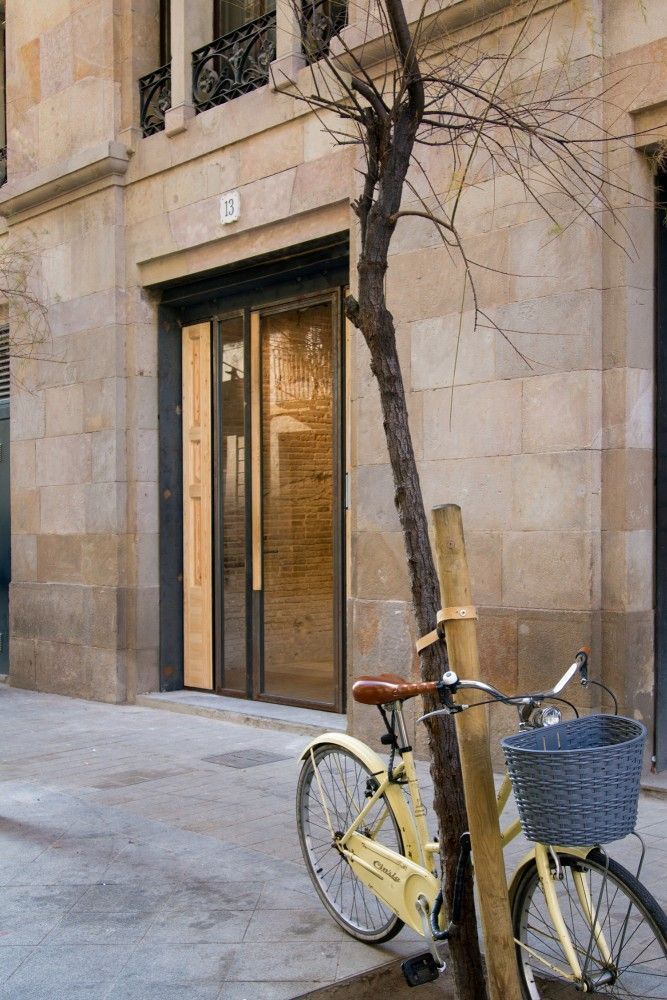 Una bicicleta de color amarillo claro con una cesta de mimbre está estacionada contra un árbol delgado y sin hojas.