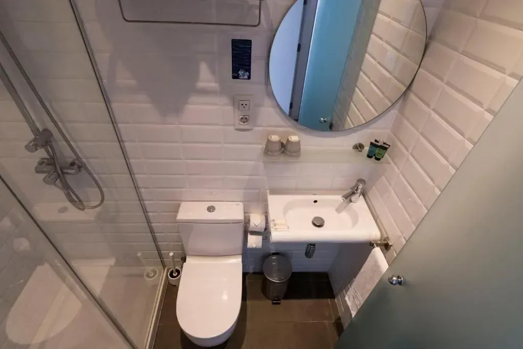 Pequeño baño moderno con ducha con mampara de cristal, inodoro blanco, lavabo de pared, espejo redondo .