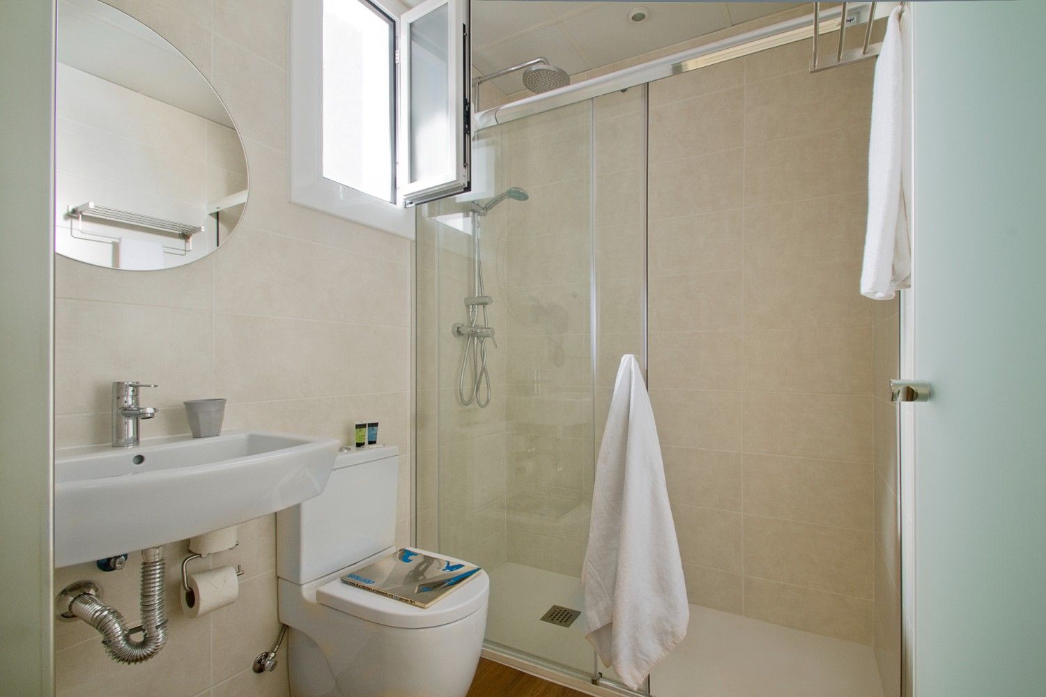 Un baño moderno con un lavabo blanco, un inodoro y una ducha con mampara de cristal y una toalla colgada en la puerta.