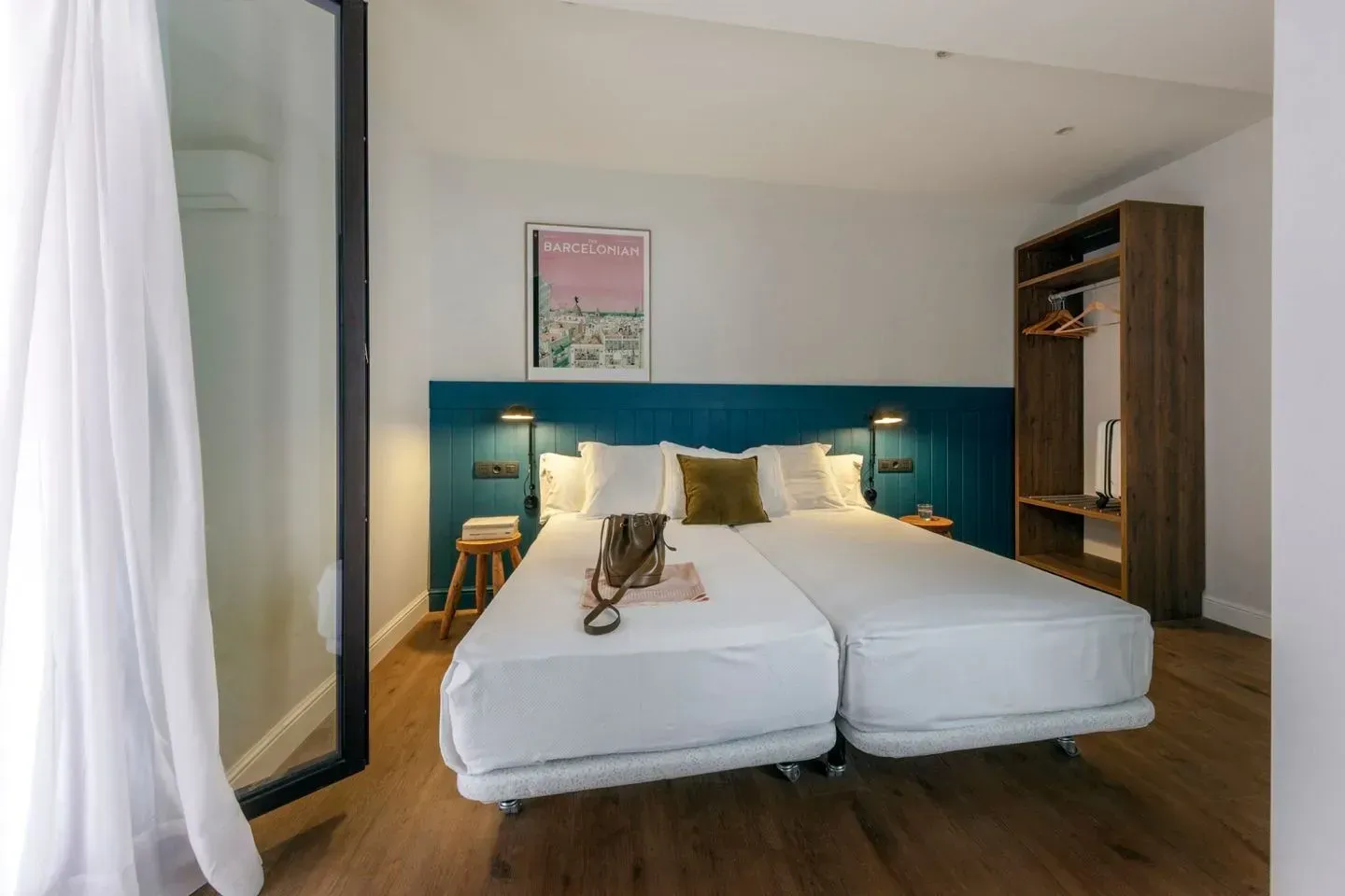 Una moderna habitación de hotel con dos camas individuales blancas, una cabecera verde azulado, piso de madera.