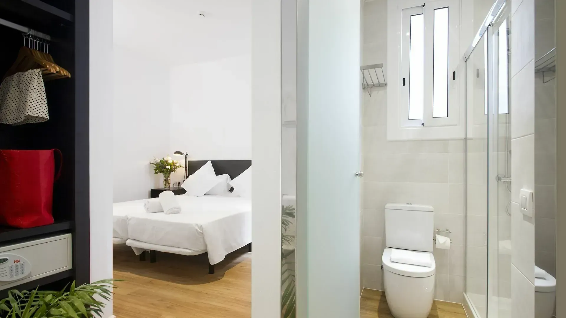 Una habitación de hotel con un dormitorio con una cama al fondo y un baño limpio con inodoro y ducha en la parte delantera.