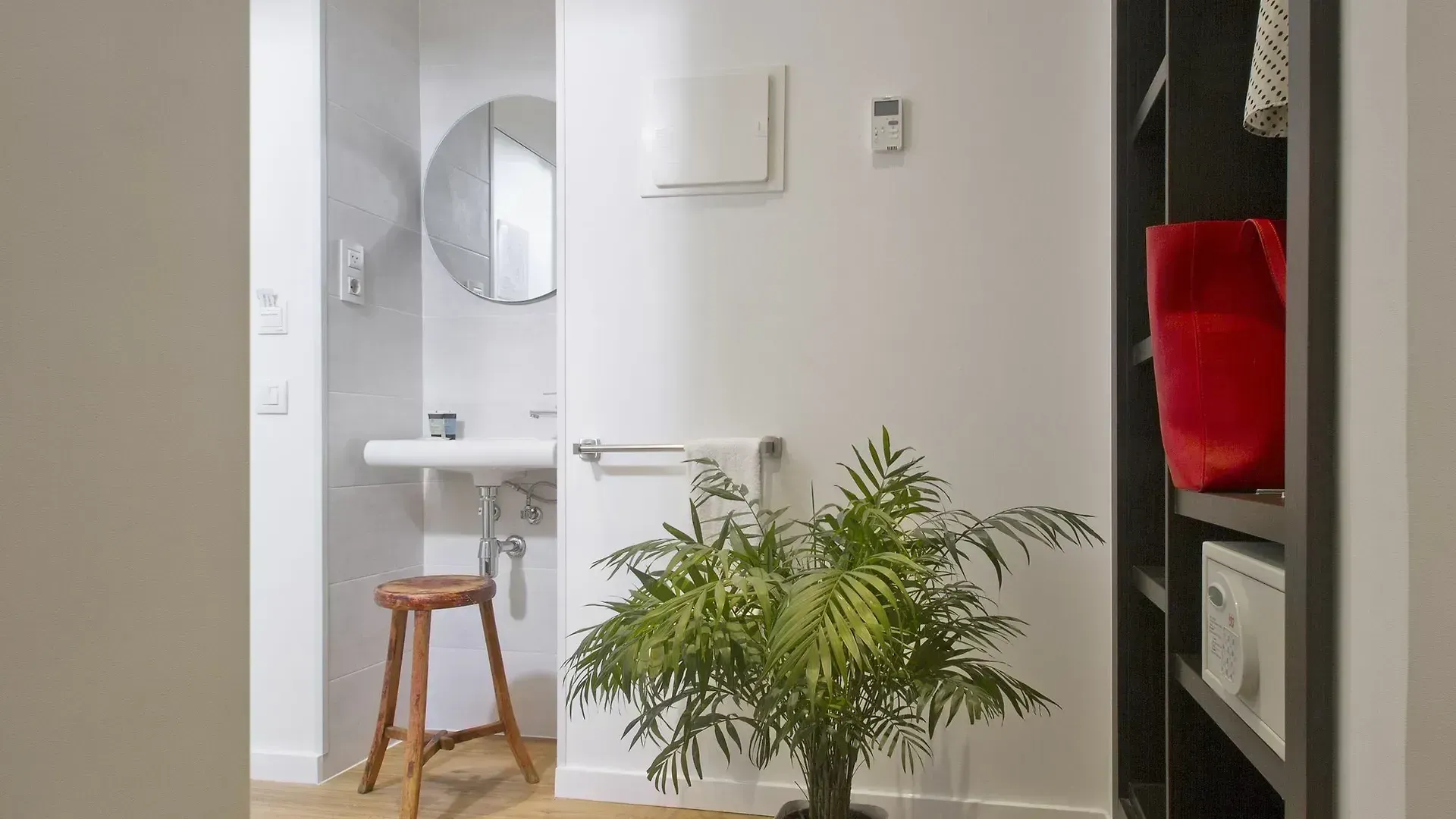 Una vista del pasillo que muestra un espejo circular sobre un lavabo blanco con un taburete de madera, una planta en maceta.