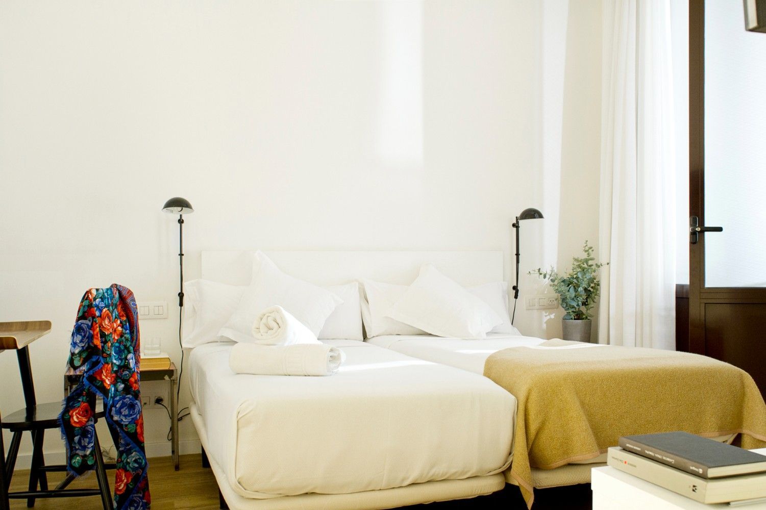 Una luminosa habitación de hotel con dos camas individuales blancas, una manta amarilla, lámparas de noche.