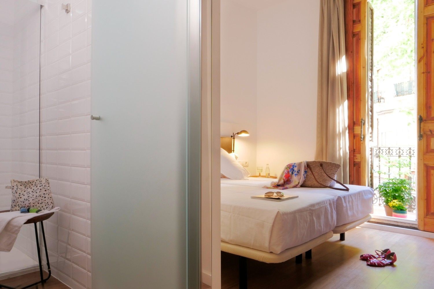 Una vista desde un baño de azulejos que da a un dormitorio de hotel luminoso con dos camas individuales.