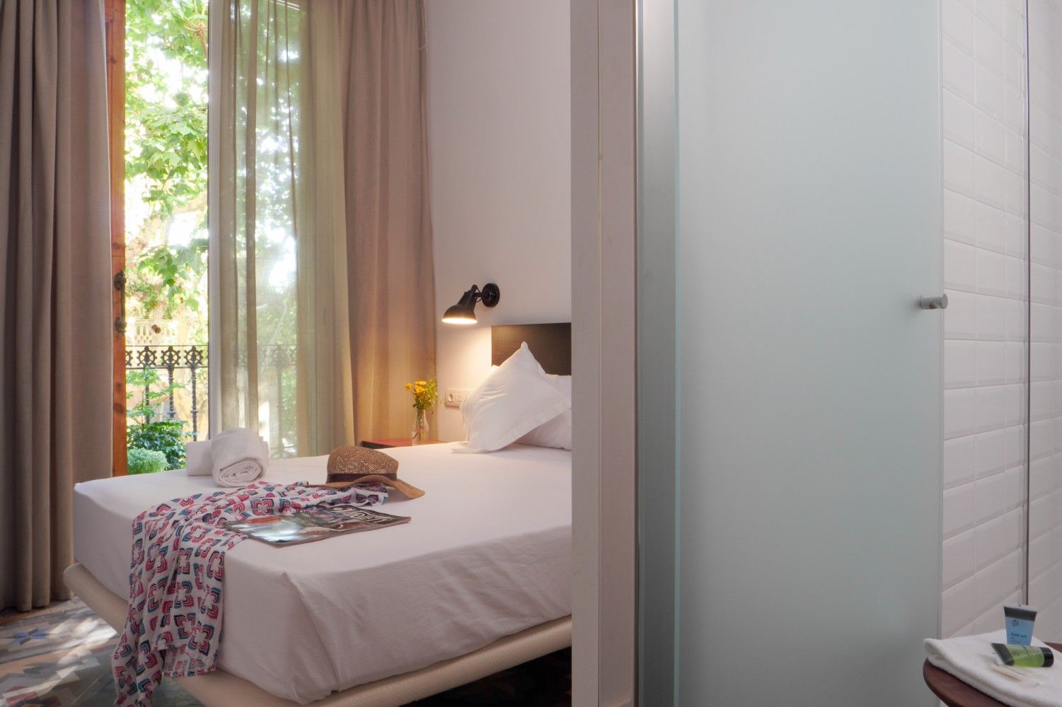 Un dormitorio de hotel luminoso con una cama blanca cuidadosamente hecha, una lámpara de noche.