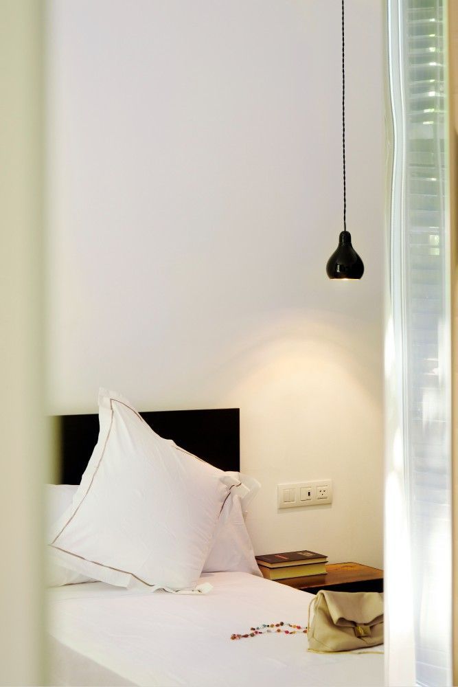 Una cama blanca con cabecera negra, almohada blanca, lámpara colgante y una pequeña mesita de noche de madera.