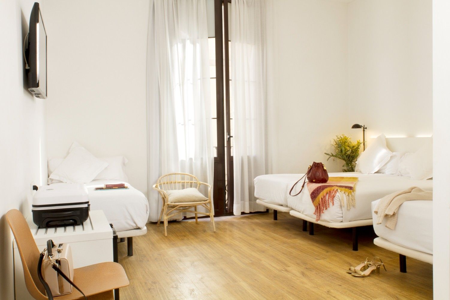 Una habitación de hotel moderna y luminosa con dos camas, una pequeña zona de estar con una silla de mimbre .