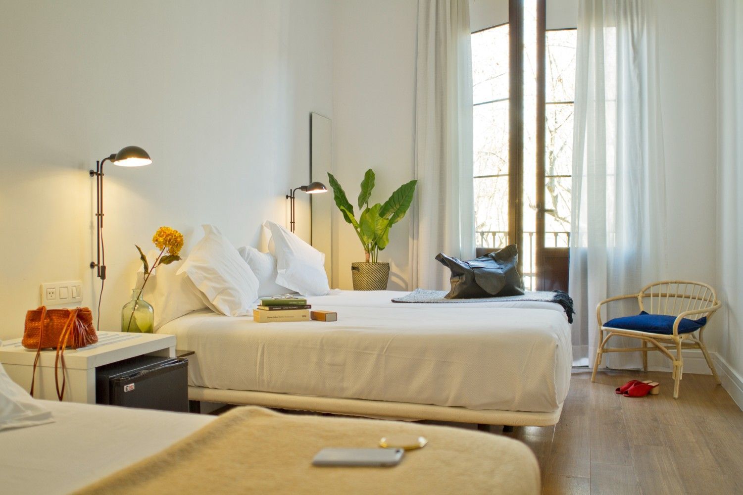 Una habitación de hotel luminosa y minimalista con dos camas, sábanas blancas, lámparas de lectura montadas en la pared.