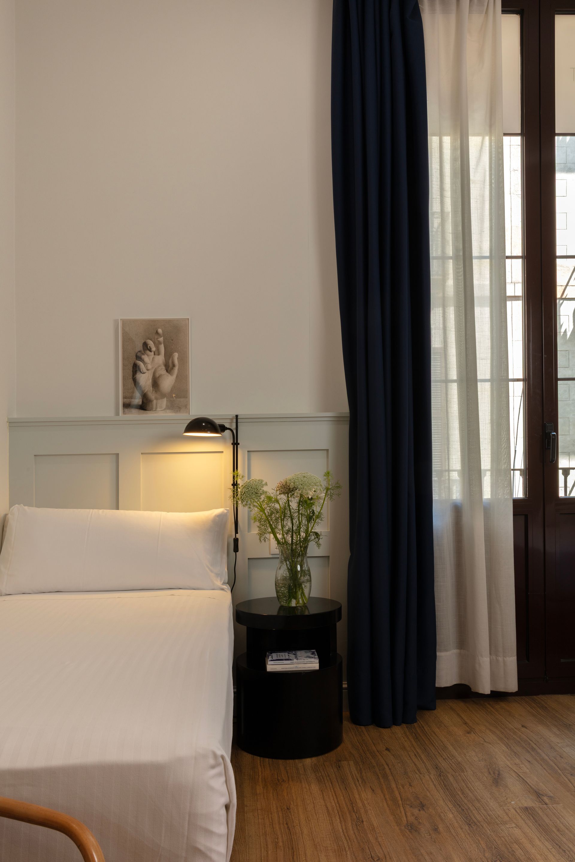 Dormitorio minimalista con cama blanca, cortinas azul marino, lámpara de noche y suelo de madera.