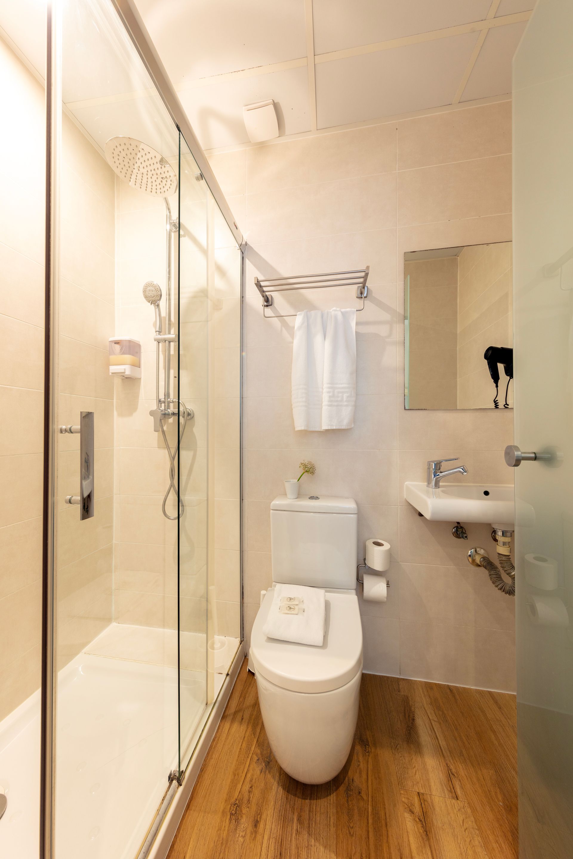 Baño accesible con ducha a ras de suelo, inodoro y lavabo sobre suelo con aspecto de madera.