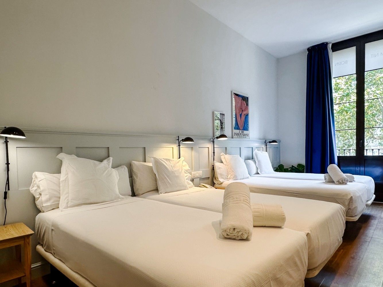 Una luminosa habitación de hotel con dos camas blancas, paredes claras, suelo de madera.