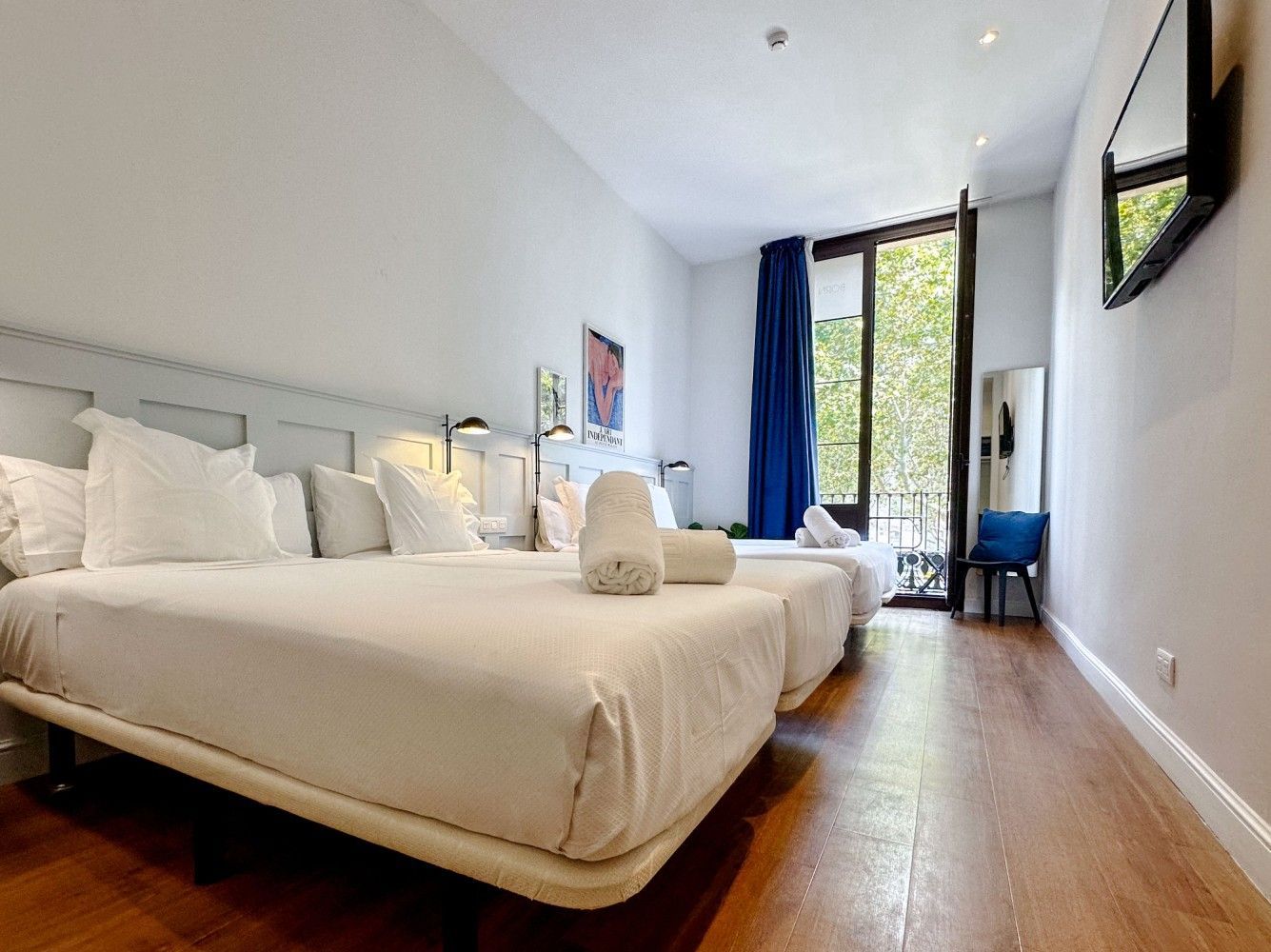 Una moderna habitación de hotel con dos camas blancas, pisos de madera, una gran ventana con cortinas azules.