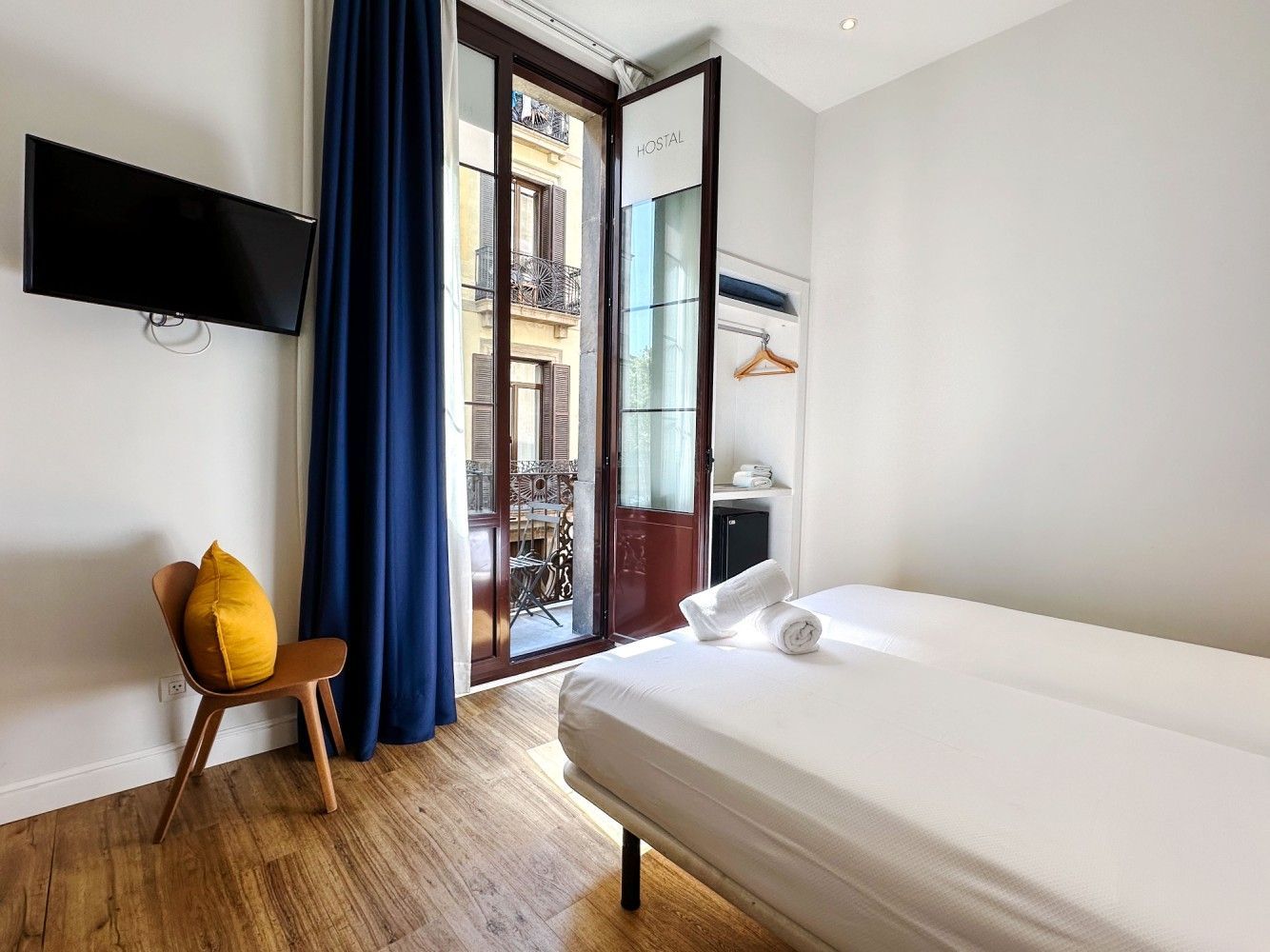 Un dormitorio minimalista con una cama, una silla de madera con una almohada amarilla,.