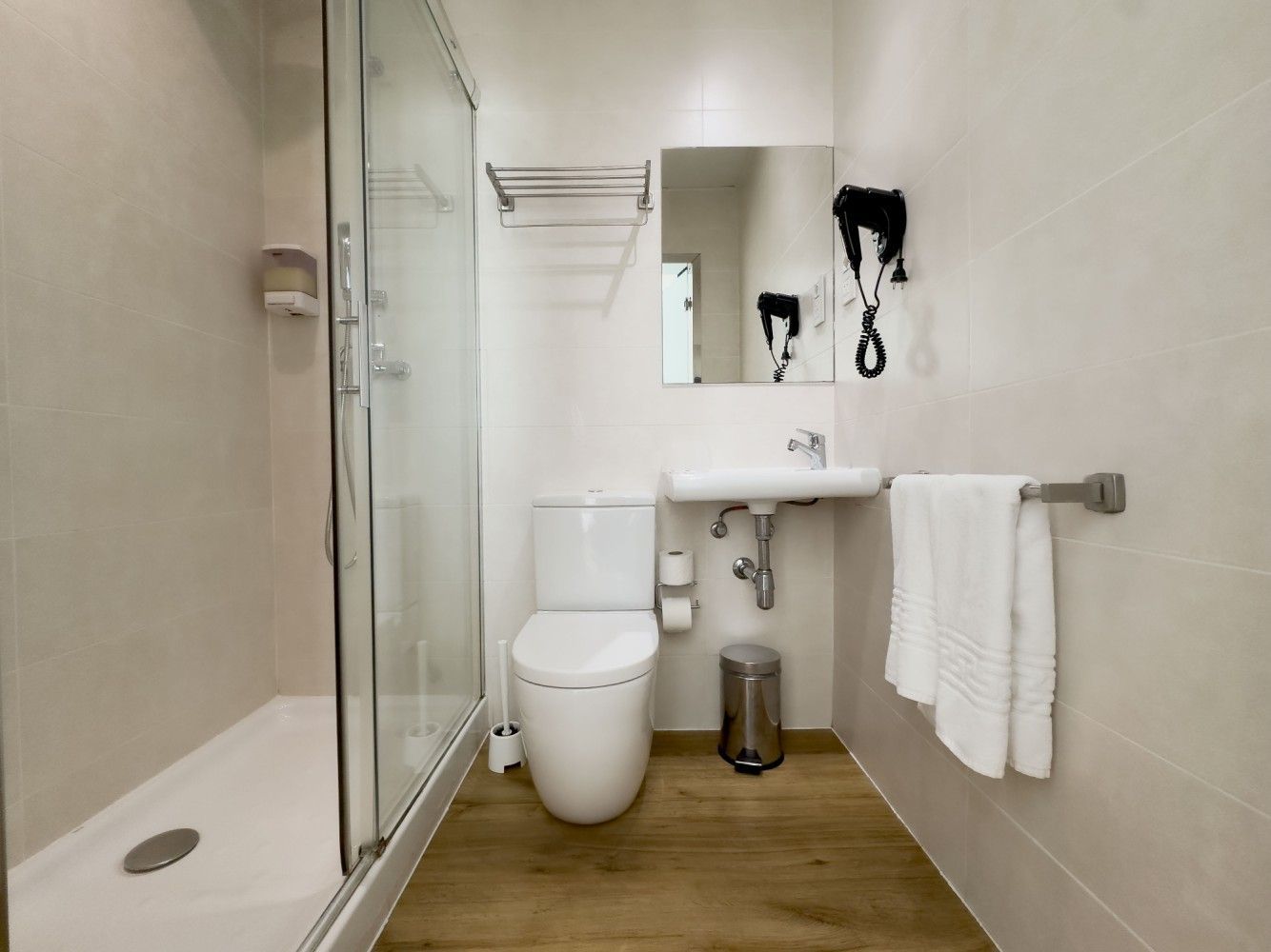 Un moderno baño de hotel con ducha con mampara de cristal, un inodoro blanco, un lavabo montado en la pared .