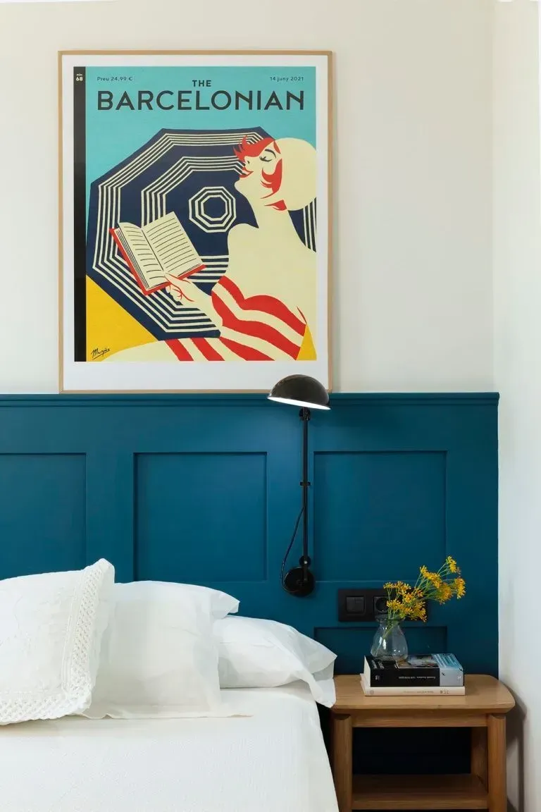 Un dormitorio con una pared revestida de color verde azulado, una cama blanca, una mesita de noche de madera.