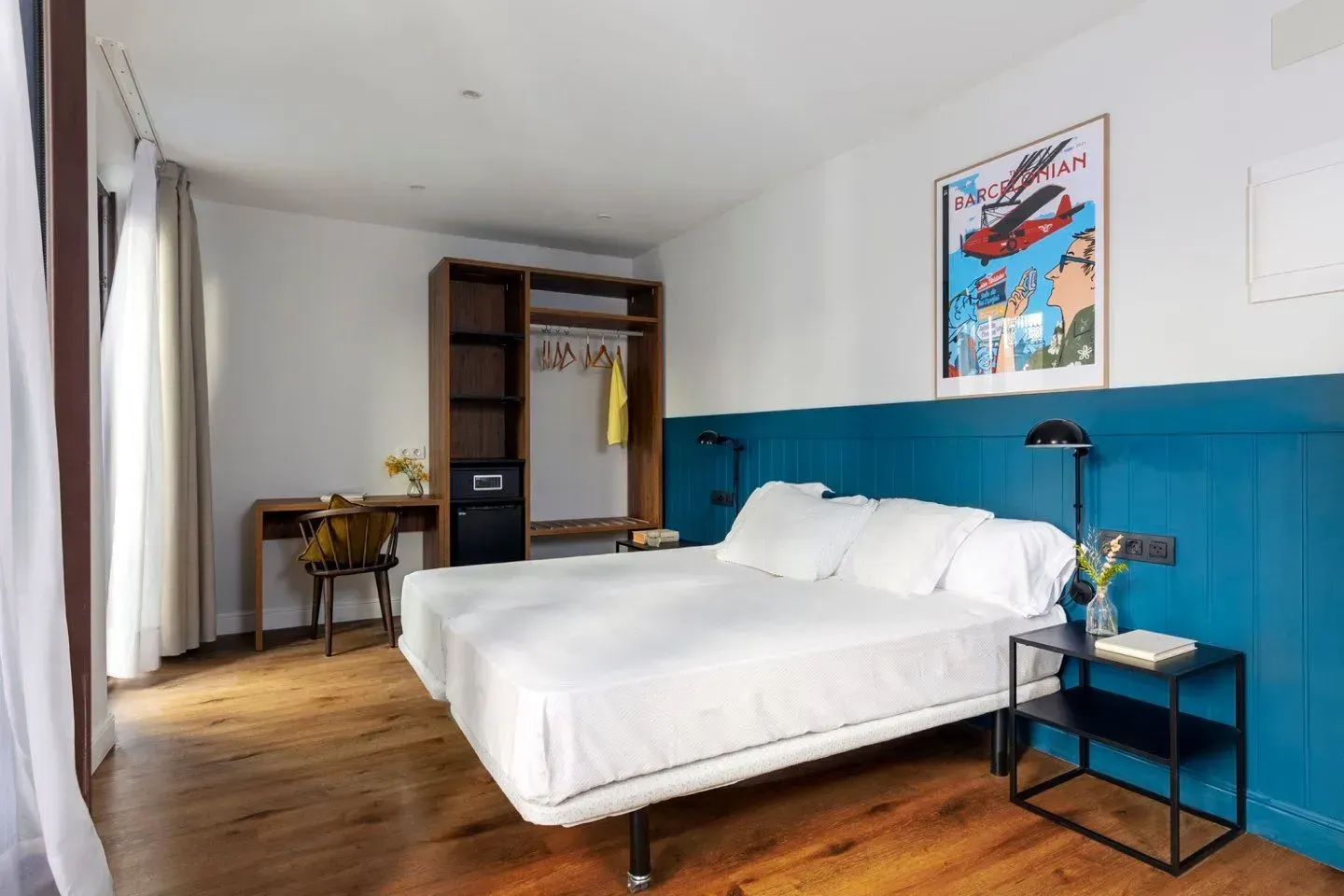 Una moderna habitación de hotel con una cama blanca, una cabecera con paneles de madera azules, un armario abierto.