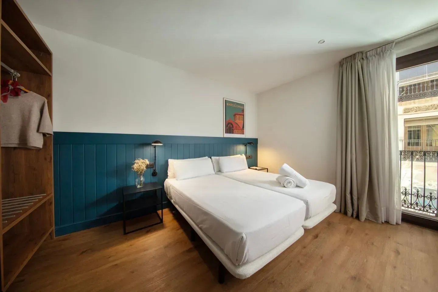 Una habitación de hotel con dos camas individuales, revestimiento de madera azul, un armario de madera abierto.