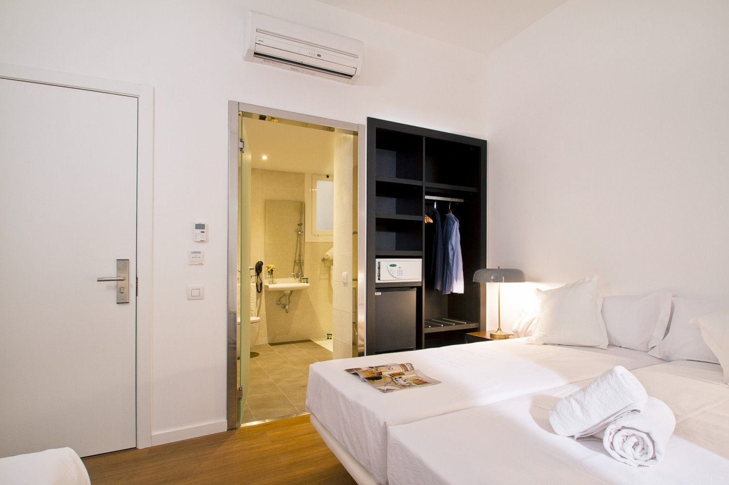 Una moderna habitación de hotel con dos camas individuales blancas, un armario negro abierto.