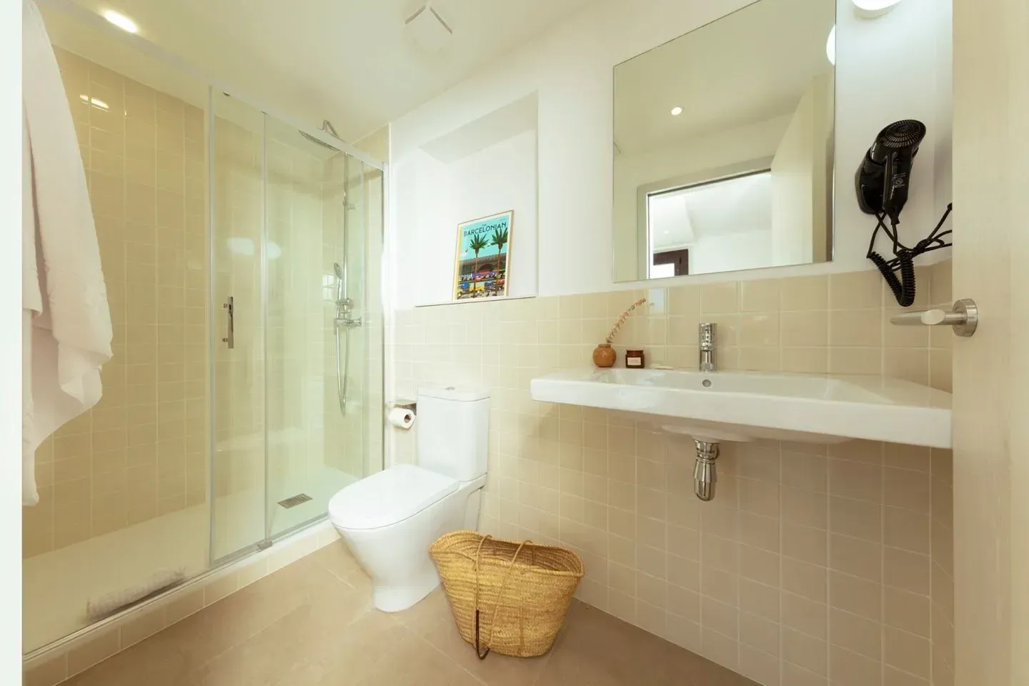Un baño moderno y luminoso con ducha con mampara de cristal, inodoro blanco y lavabo de pared con espejo grande.