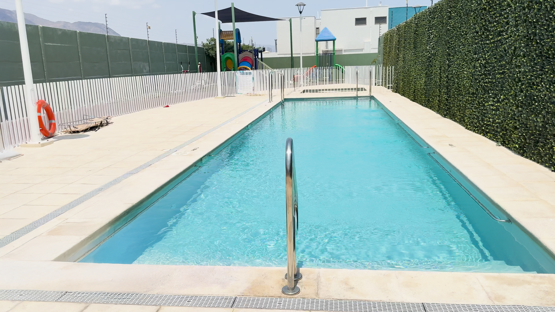 Una gran piscina con un parque infantil al fondo.