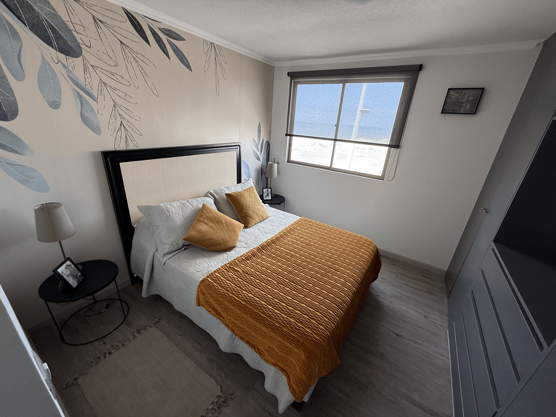 Un dormitorio con cama, mesita de noche, lámpara y ventana.