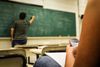 A man is writing on a blackboard in a classroom.
